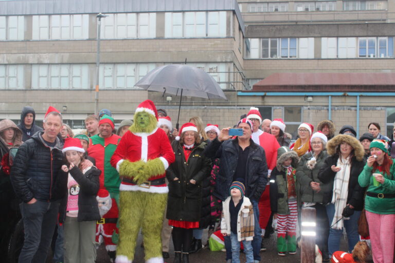 The Grinch and other festively dressed people gathered in front of a hospital